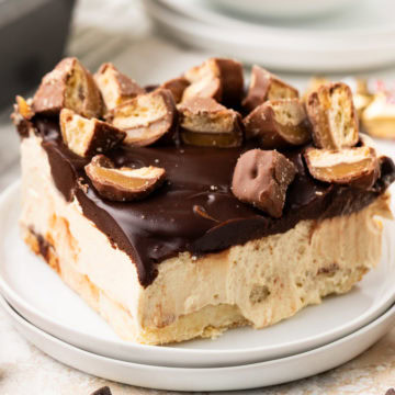 Twix cheesecake bars topped with chocolate ganache and chopped candy bars.