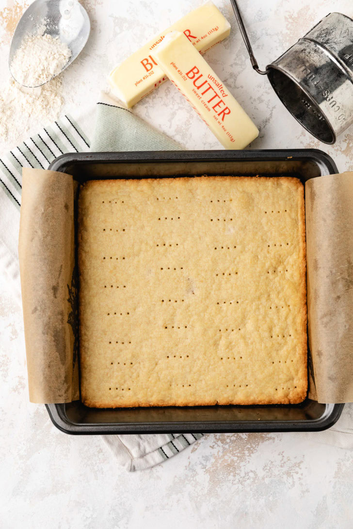 A shortbread crust fills a square pan lined with parchment paper.