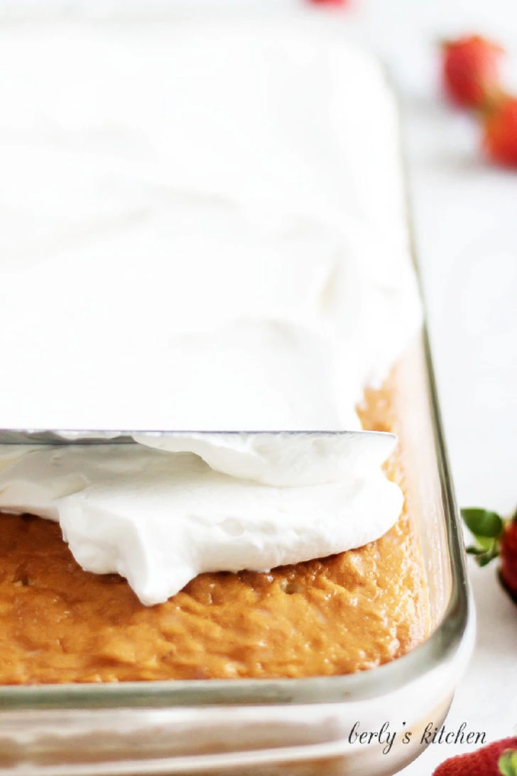 Spreading homemade whipped cream over tres leches cake in a glass baking dish.