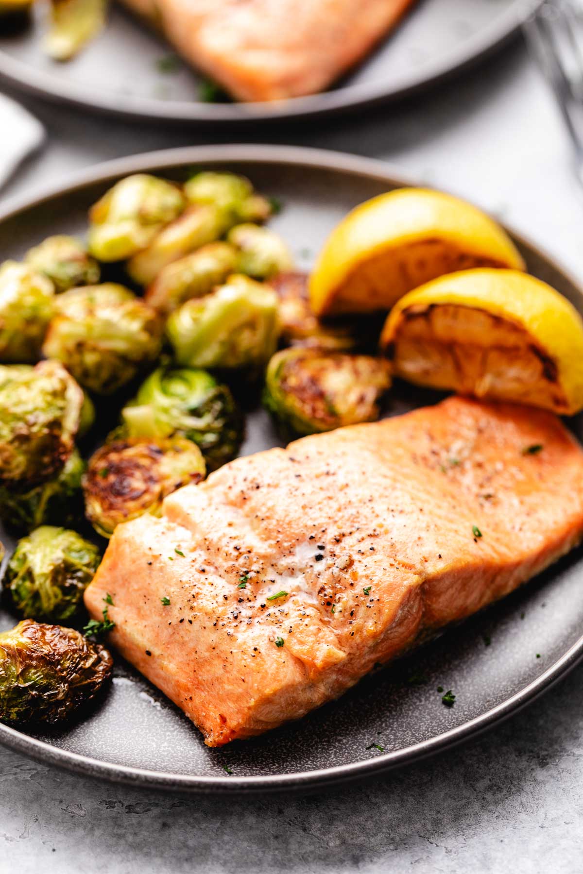 Piece of air fryer salmon on a gray plate next to sauteed brussels sprouts.