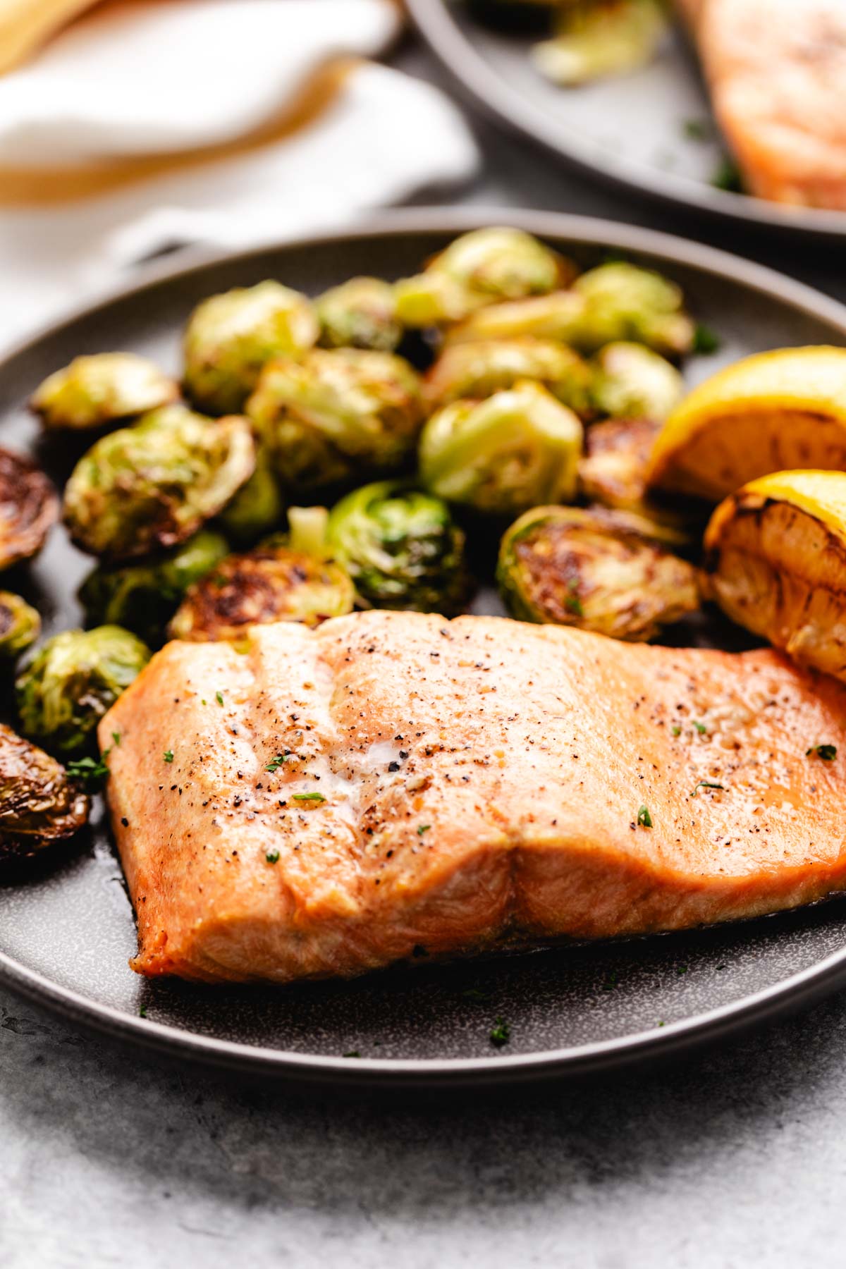 Side view of air fried salmon on a dark plate next to lemons.