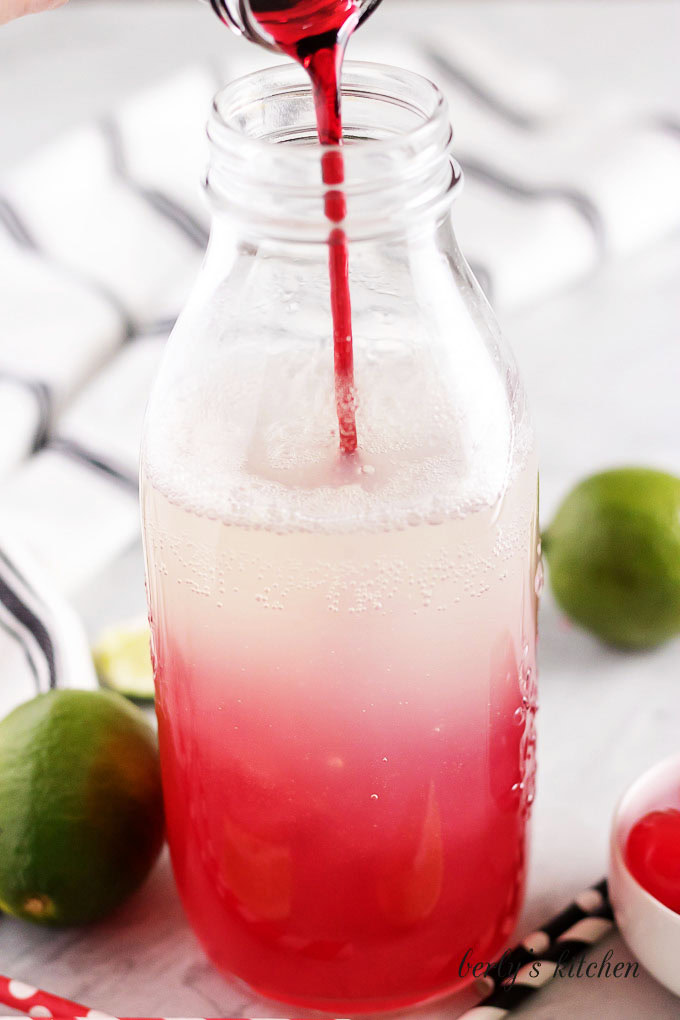 Cherry simple syrup being added to a jar of lemon lime soda and lime juice.