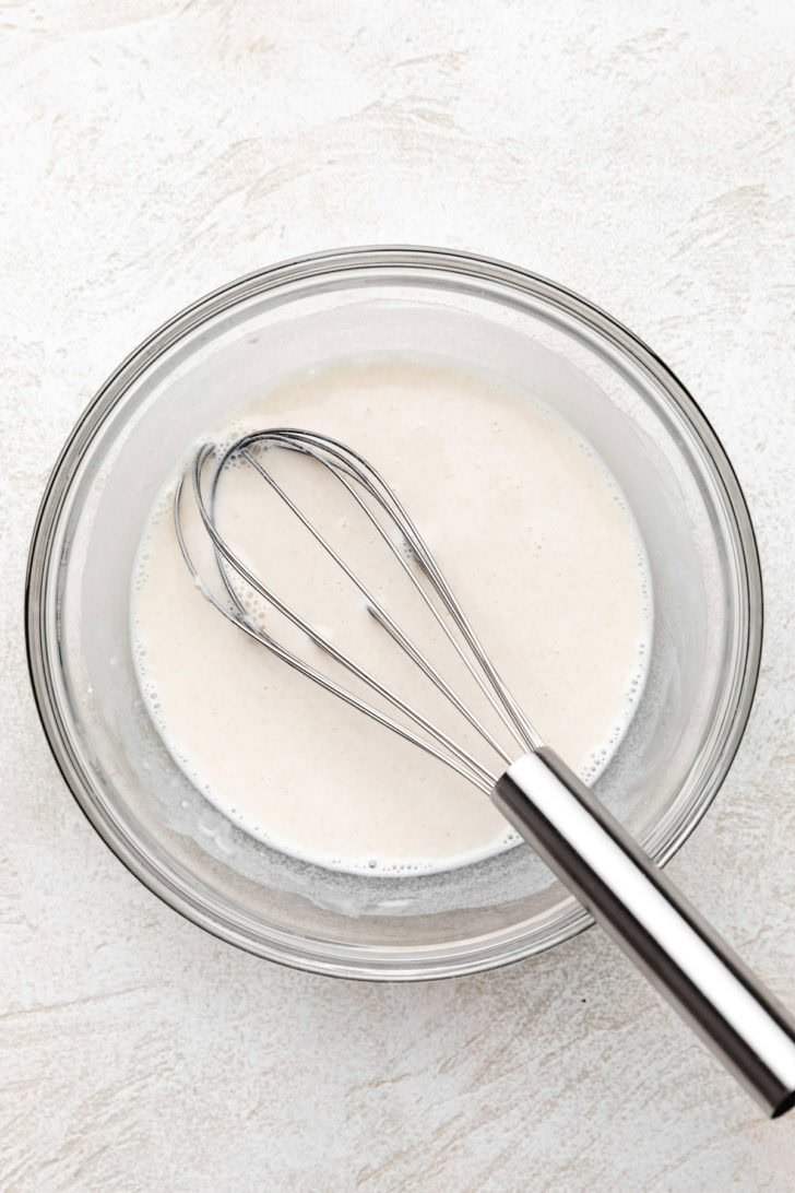 Bowl of milk and flour with a metal whisk.