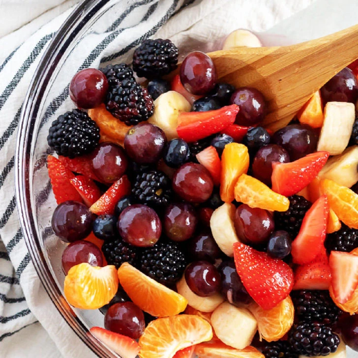 Overhead view of fresh fruit salad in a glass mixing bowl.