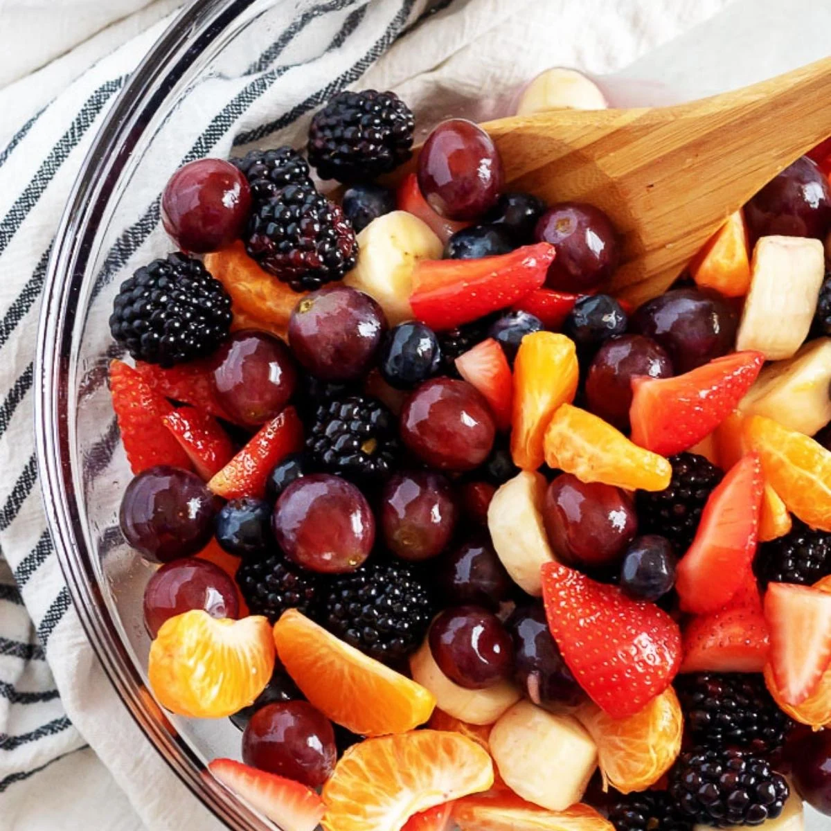 Overhead view of fresh fruit salad in a glass mixing bowl.