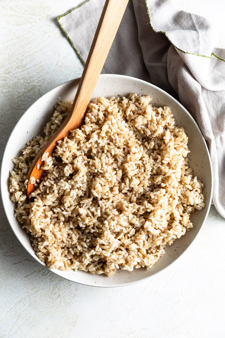 Brown rice in a serving bowl with a wooden spoon.