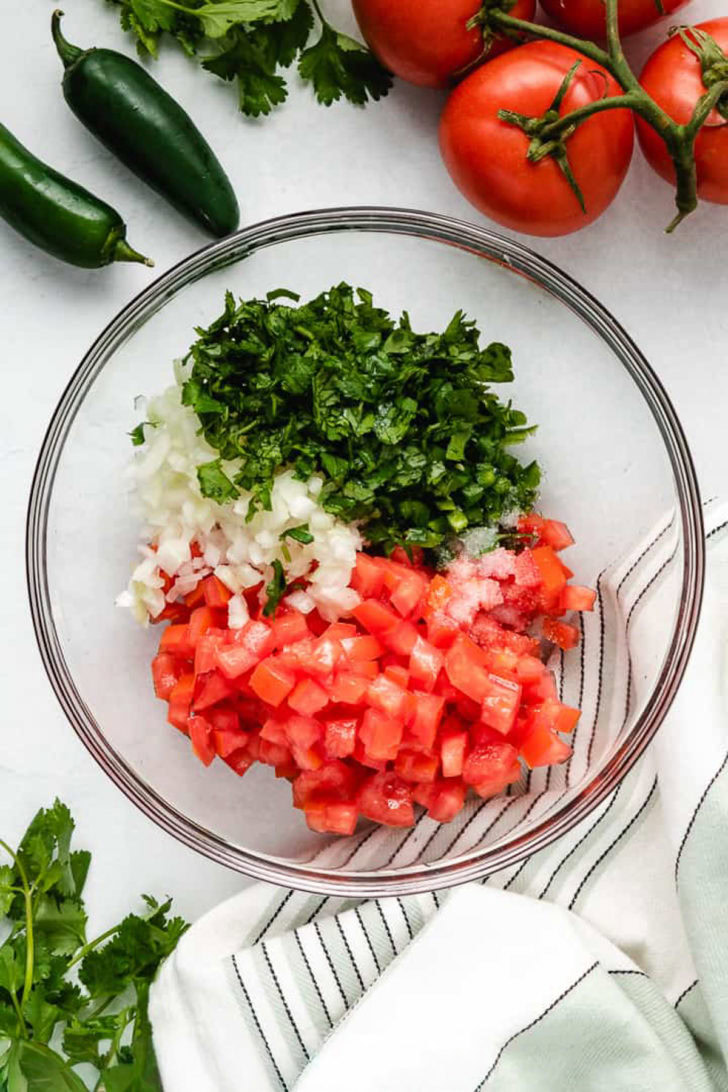 Diced tomatoes, cilantro, salt, and diced onions in a glass bowl.