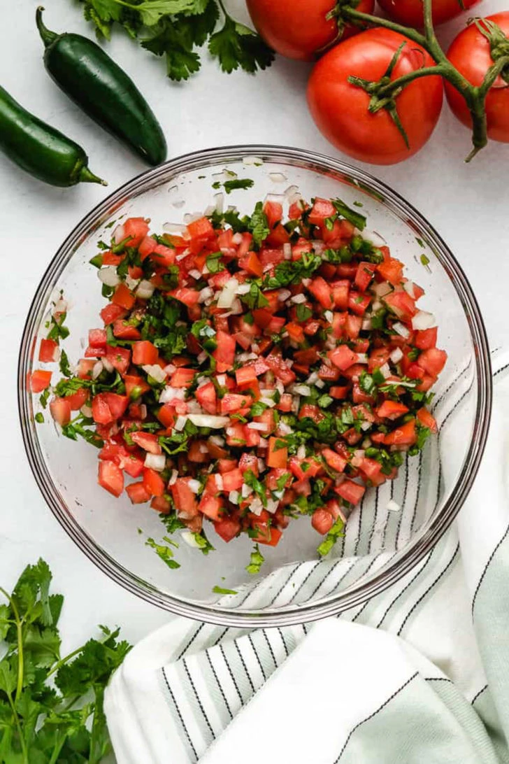 Ingredients for pico de gallo mixed in a glass mixing bowl.