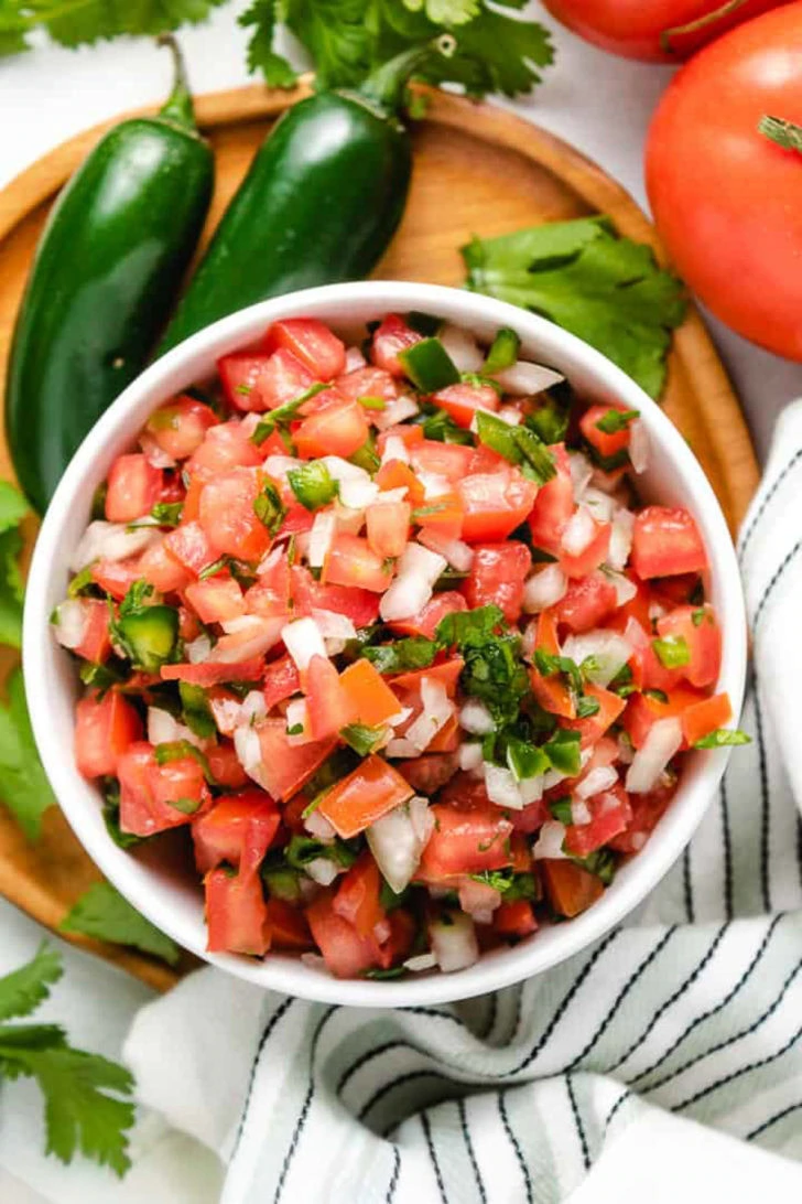 Diced pico de gallo in a white bowl next to a striped towel.