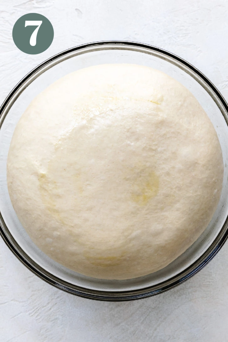 Puffy, risen brioche dough in a glass mixing bowl.