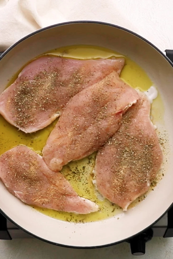 Seasoned chicken breasts cooking in a skillet.