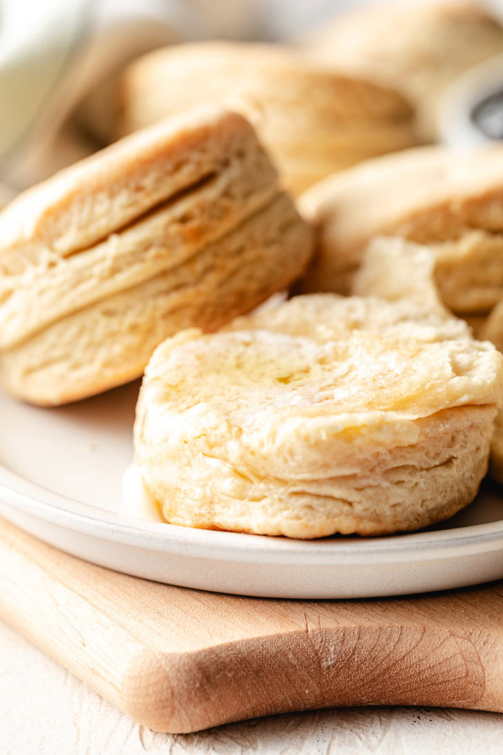Close up of a tall, flaky homemade biscuit with butter on top, showing distinct layers on the side.