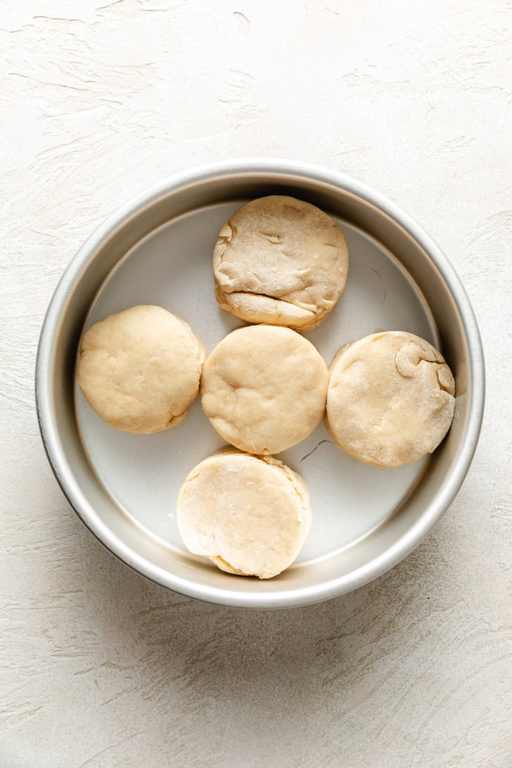 Five unbaked biscuits placed touching each other in a round cake pan.