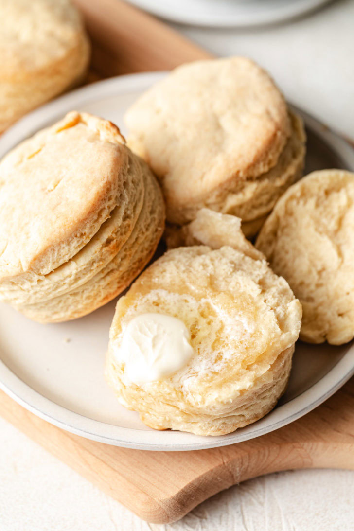 Close up of a flaky homemade buttermilk biscuit with butter on a white plate, showing layers on the side.