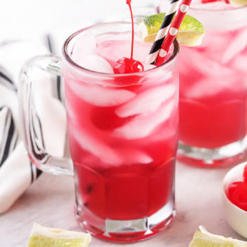 Glass mug filled with cherry limeade next to fresh lime wedges.