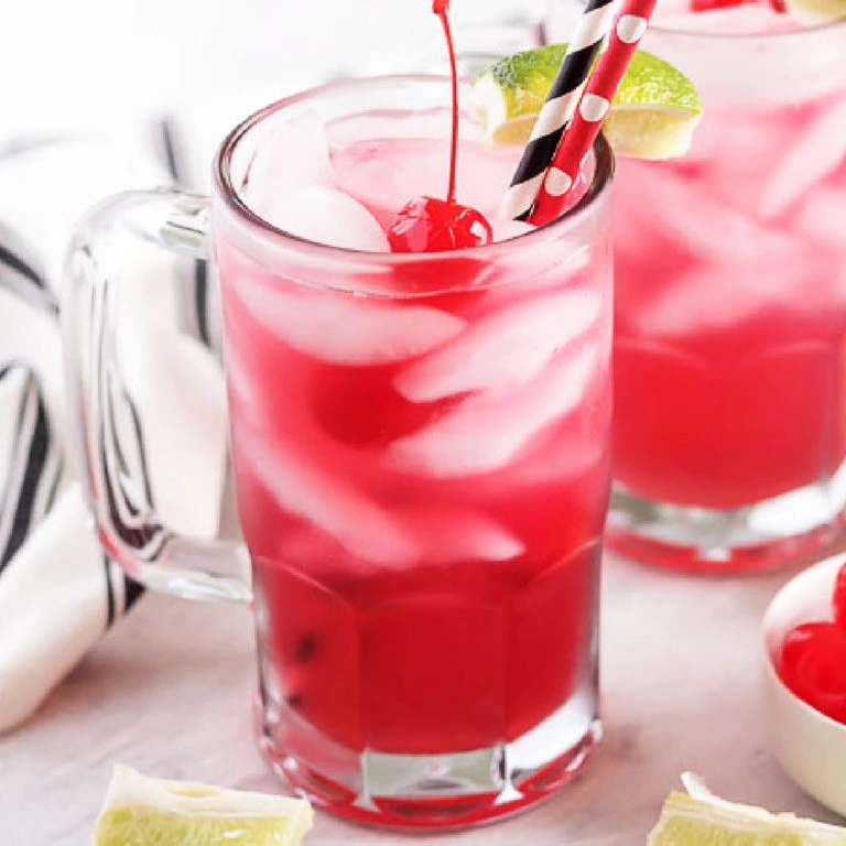 Glass mug filled with cherry limeade next to fresh lime wedges.