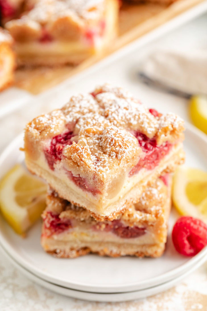 Lemon raspberry crumb bars stack on white plates and sprinkled with powdered sugar.