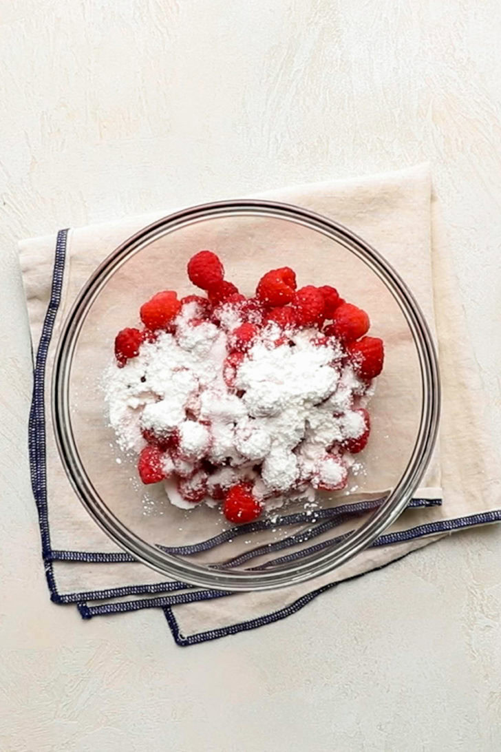 Fresh raspberries, granulated sugar, and cornstarch in a glass mixing bowl.
