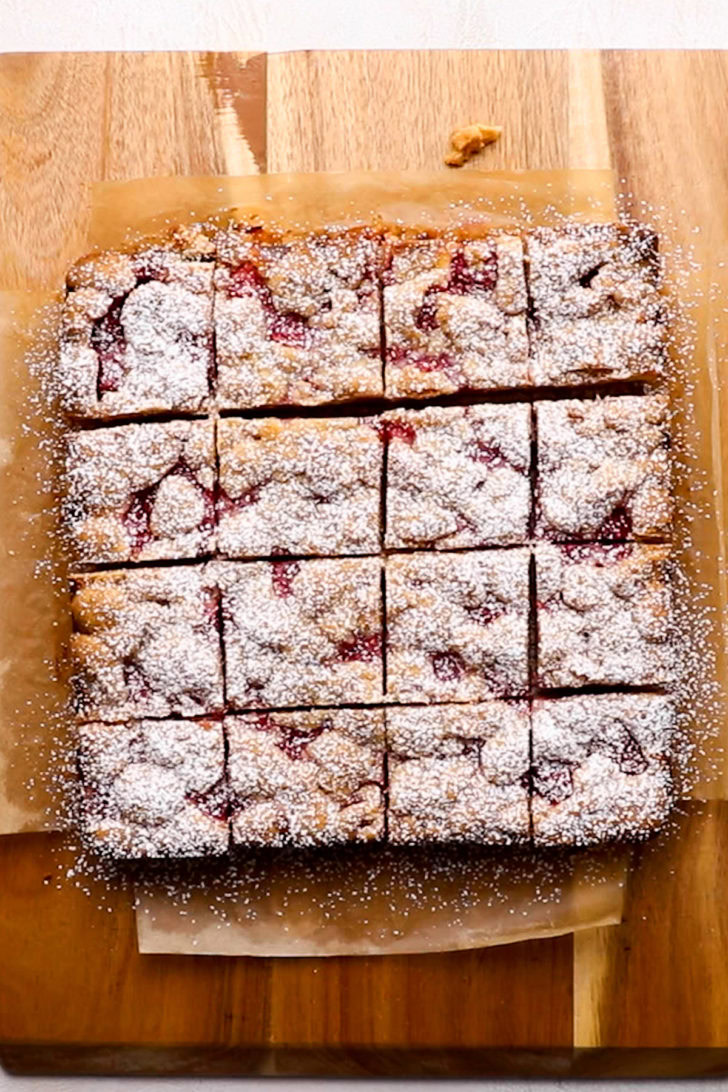 Sliced lemon raspberry bars on a cutting board dusted with powdered sugar.