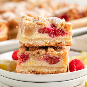 Close up view of a stack of lemon raspberry crumb bars next to fresh berries on plates.