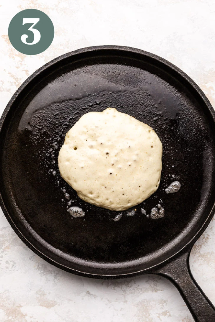 Pancake batter cooking in melted butter on a skillet.