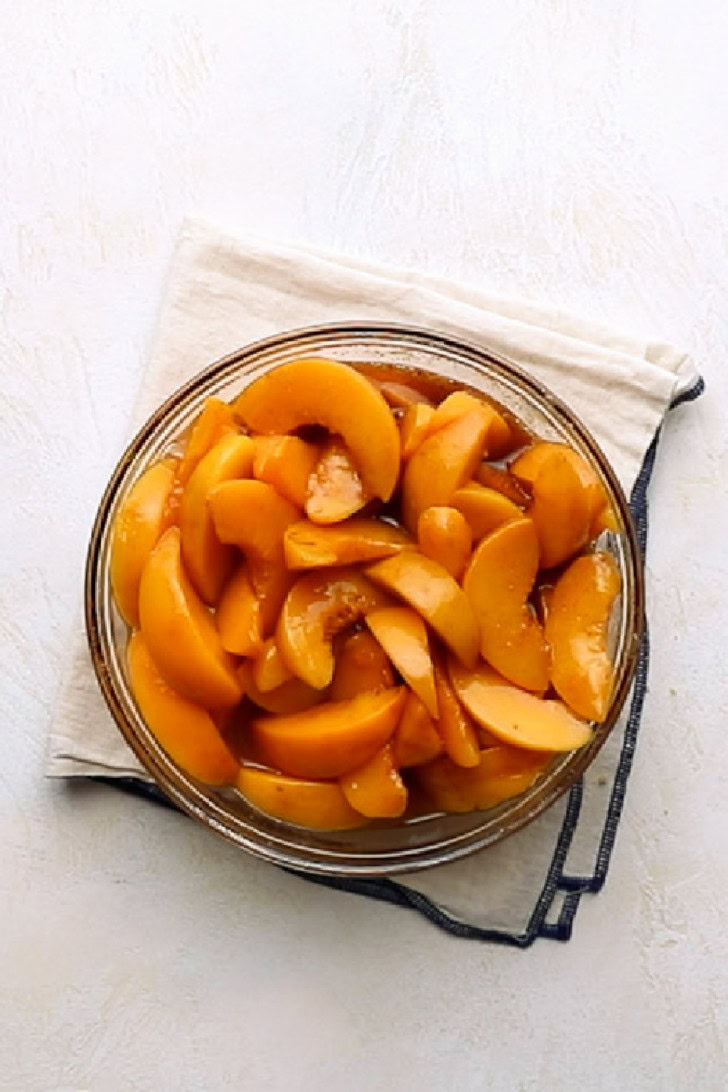 Sweetened peaches with cinnamon and syrup in a glass mixing bowl.