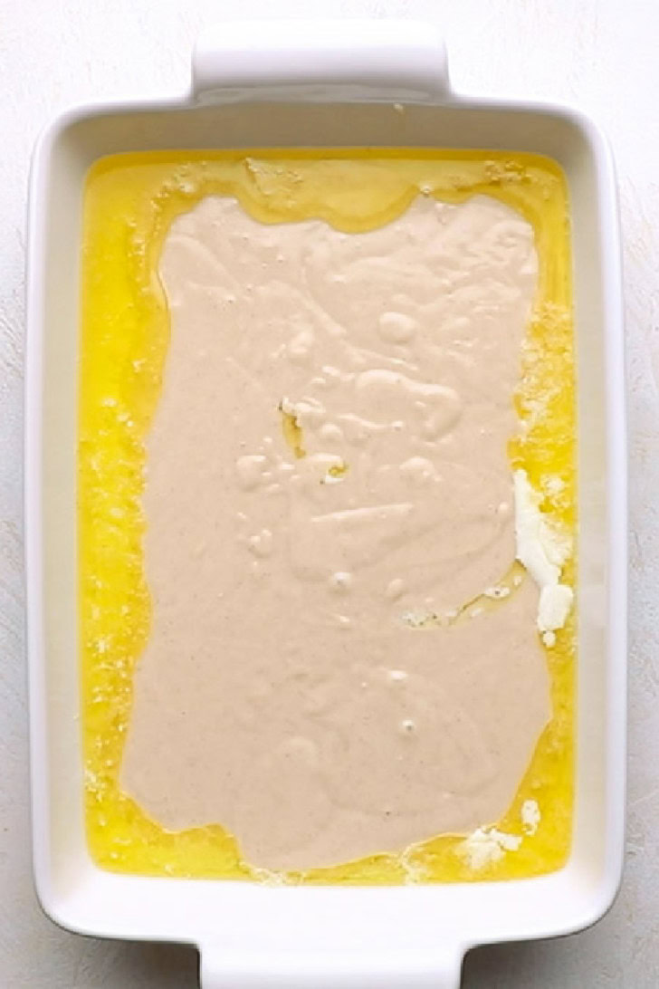 Peach cobbler batter poured over melted butter in a baking dish.