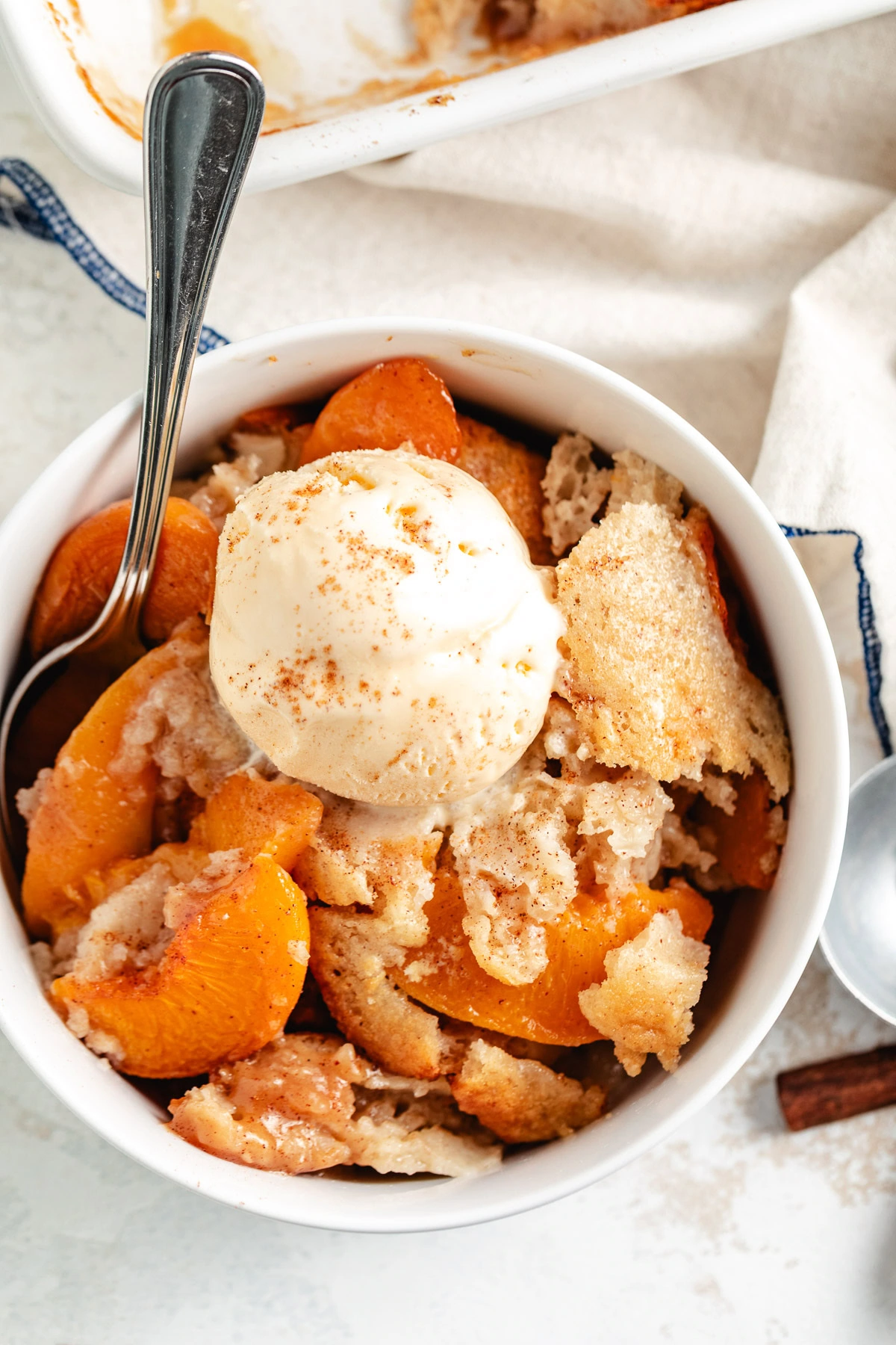 Peach dessert served in a white bowl with vanilla ice cream and cinnamon.