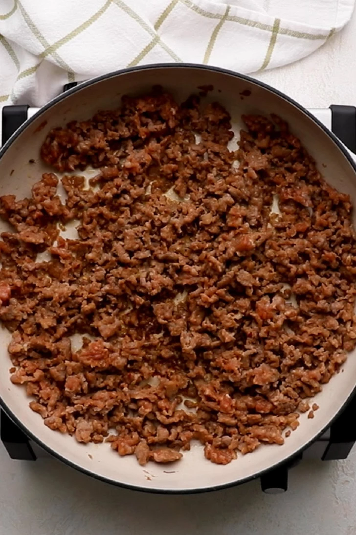 Browned Italian sausage crumbles in a skillet.