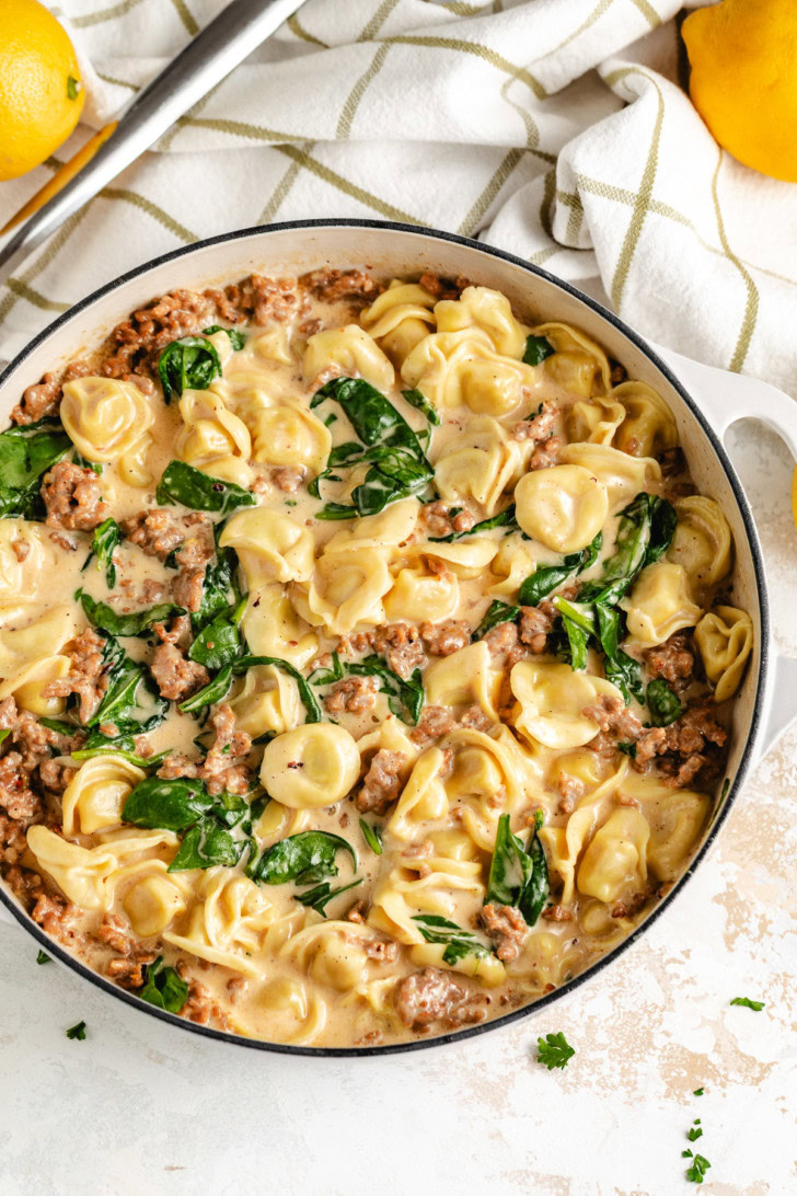 Creamy lemon sausage tortellini in a white skillet.