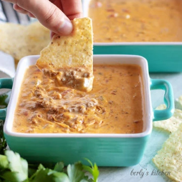 Close up view of a chip being dipped into beef queso dip.