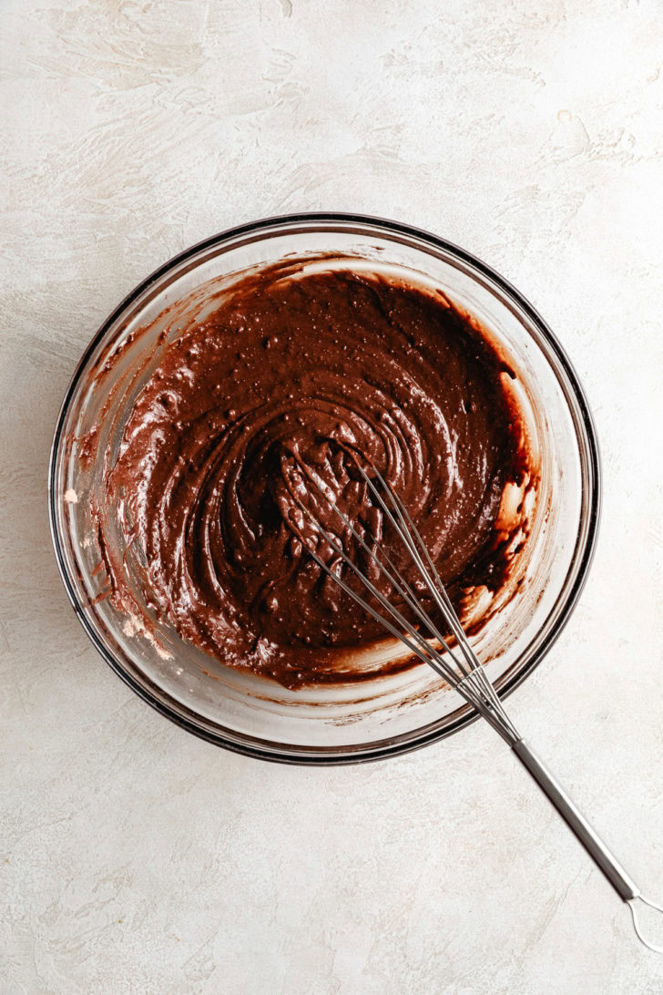 Thick chocolate brownie batter whisked together in a glass bowl.