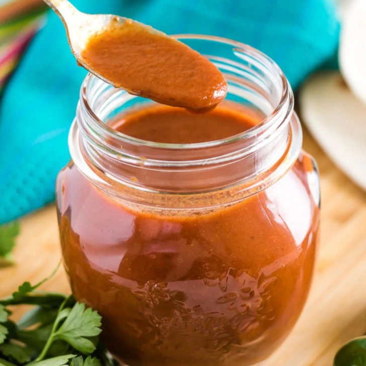 Spoon holding up enchilada sauce from a jar.