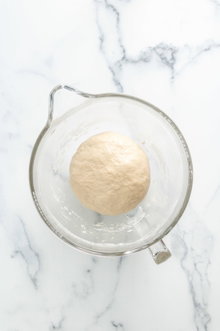 Smooth French bread dough in a glass mixing bowl.