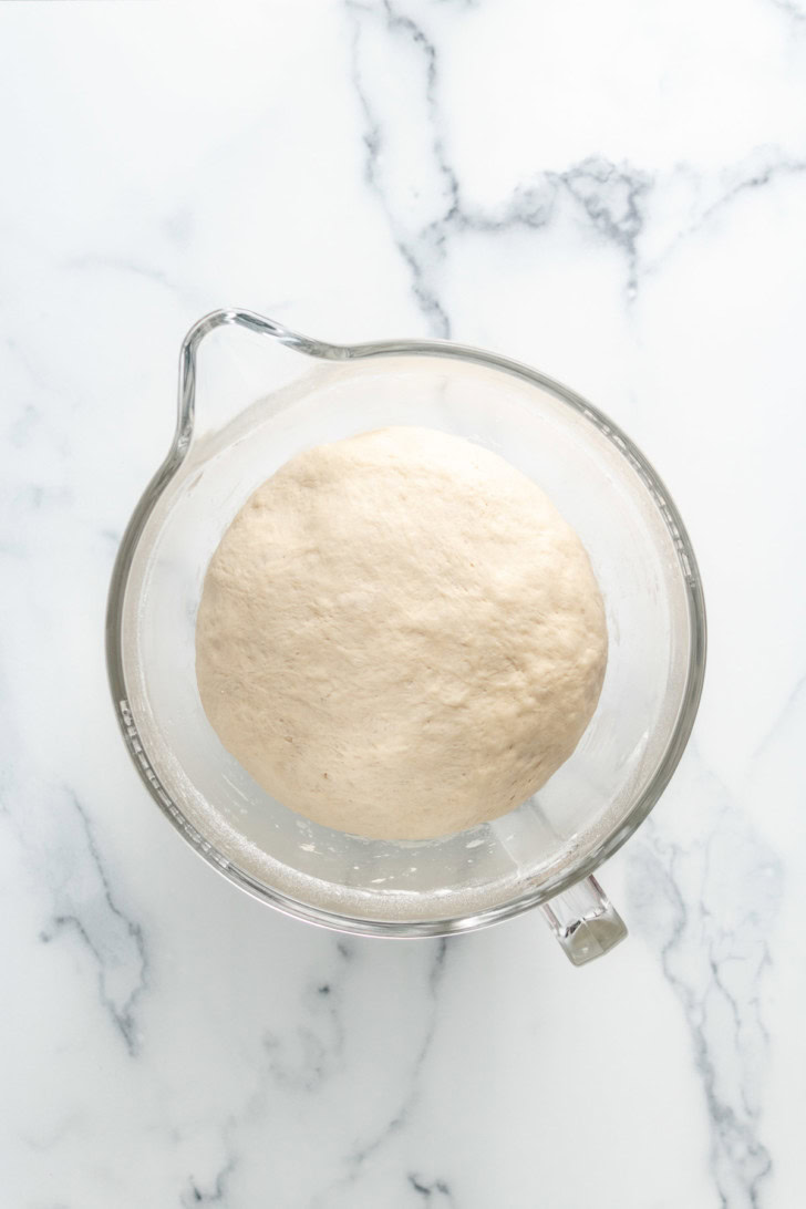 Risen dough in a glass mixing bowl.
