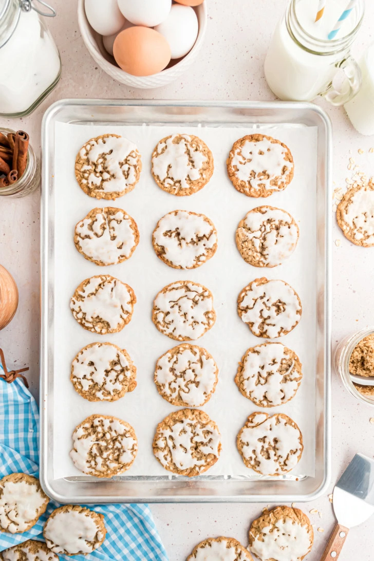 Iced oatmeal cookies arranged on a parchment-lined baking sheet.