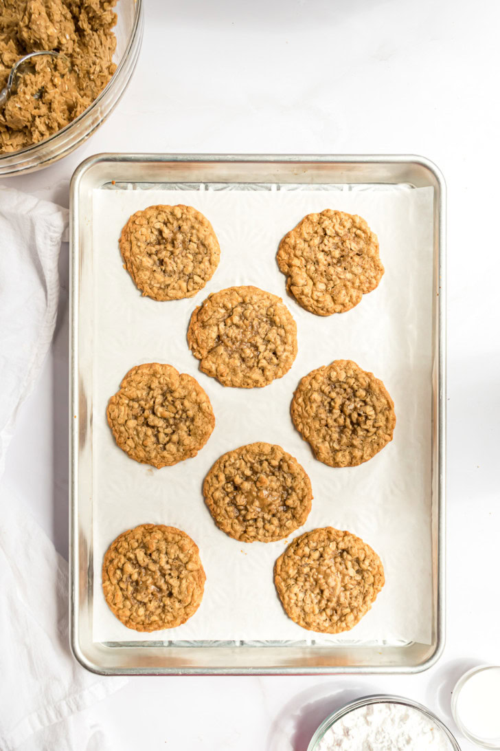 Baked oatmeal cookies cooling on a parchment-lined baking sheet.