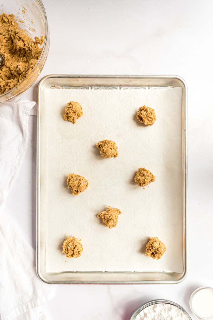 Scoops of oatmeal cookie dough spaced apart on a parchment-lined baking sheet.