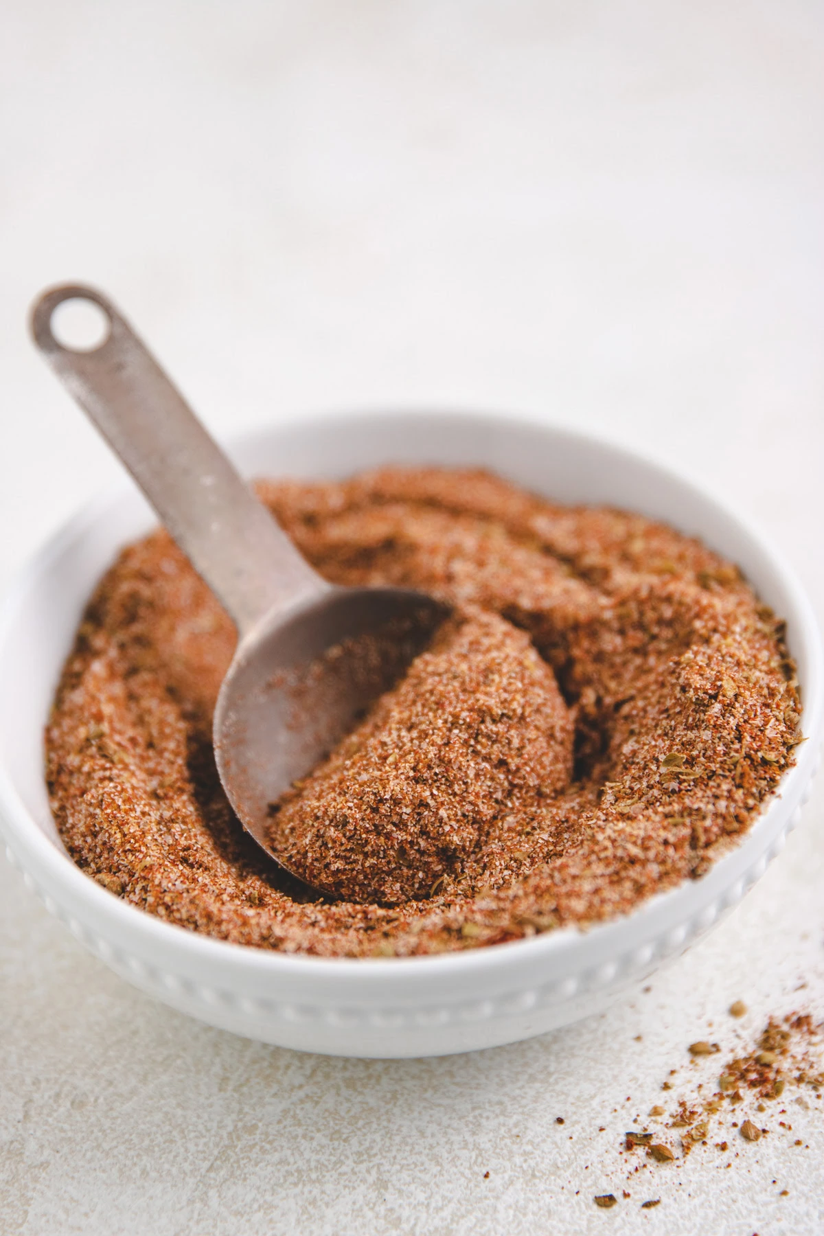 Metal spoon in a white bowl filled with taco seasoning.
