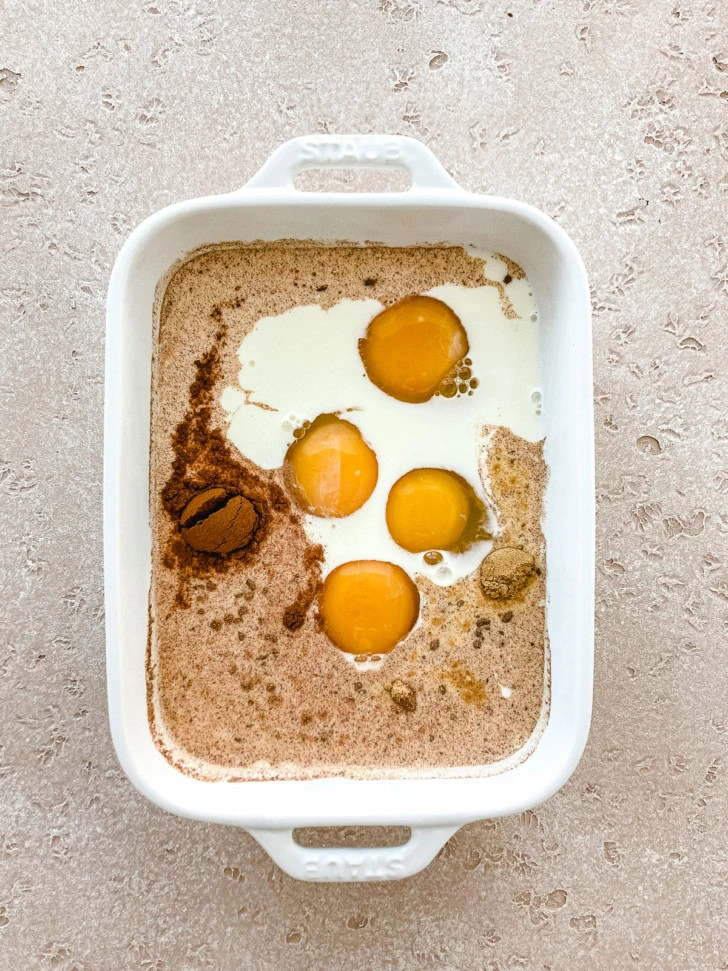 Egg and milk mixture with cinnamon and spices in a baking dish.