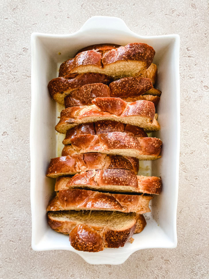 Sliced challah bread arranged in a white baking dish.