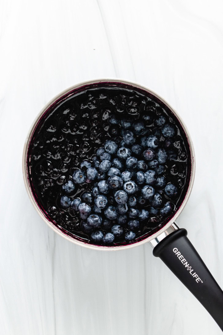 Fresh blueberries added to a pan of cooked blueberries.
