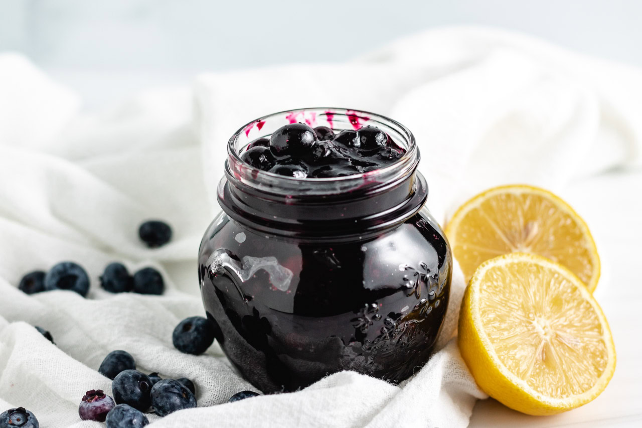 Jar of blueberry compote next to fresh lemons.