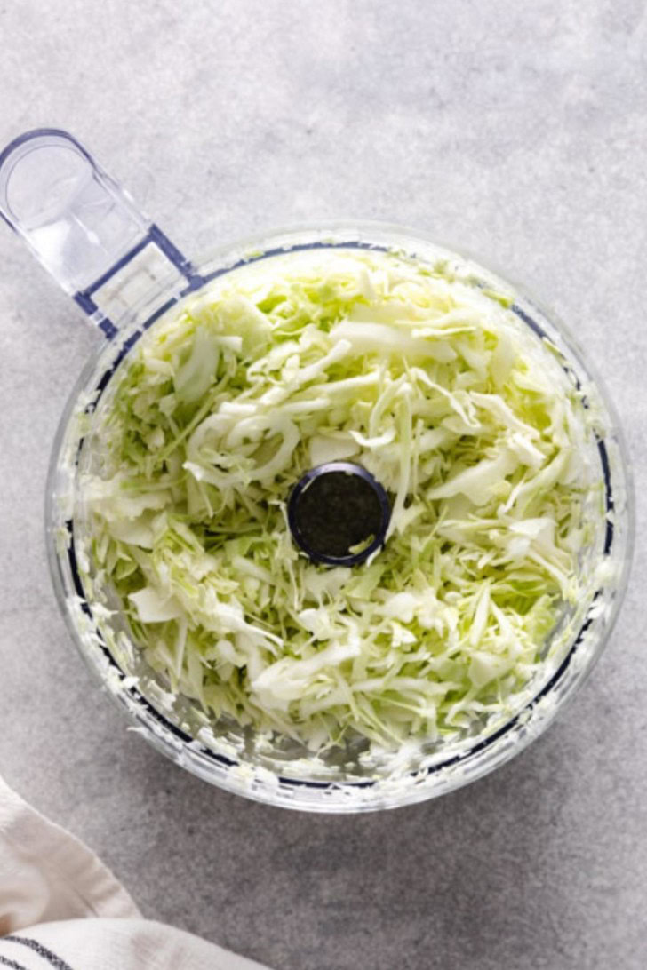 Overhead view of shredded cabbage in a food processor.