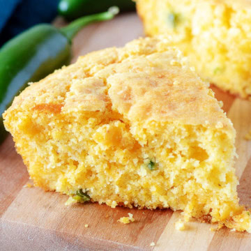 Close up view of two slices of fluffy jalapeno cornbread on a wooden cutting board.