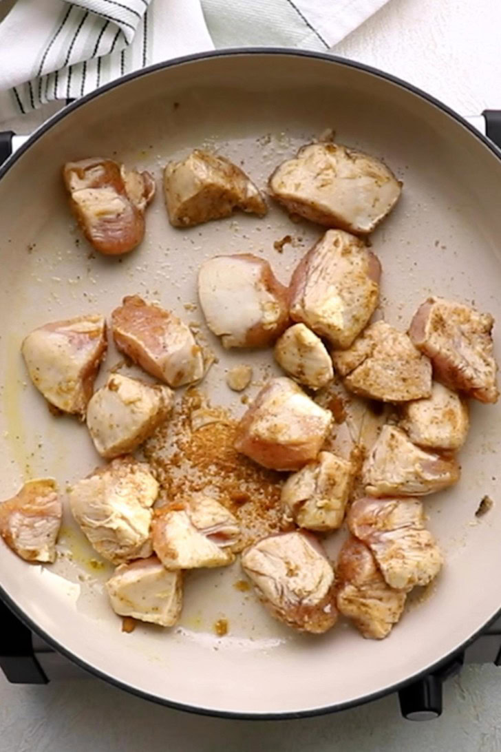Seasoned chicken pieces browning in a skillet.