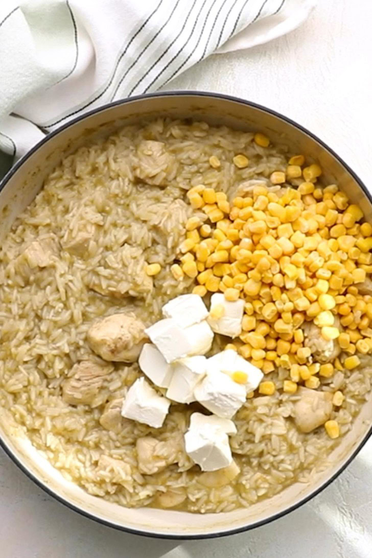 Corn and cream cheese added to chicken and rice in a skillet.