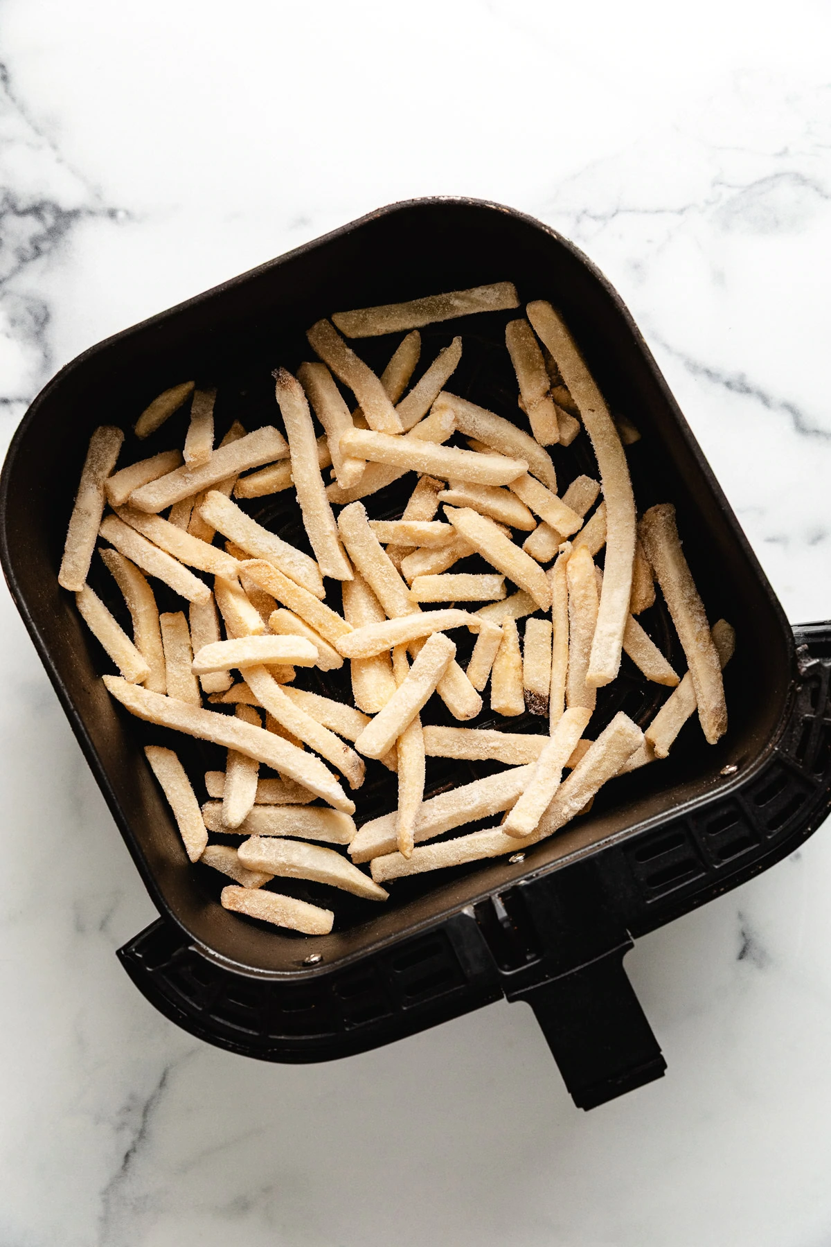 Frozen french fries in an air fryer basket.
