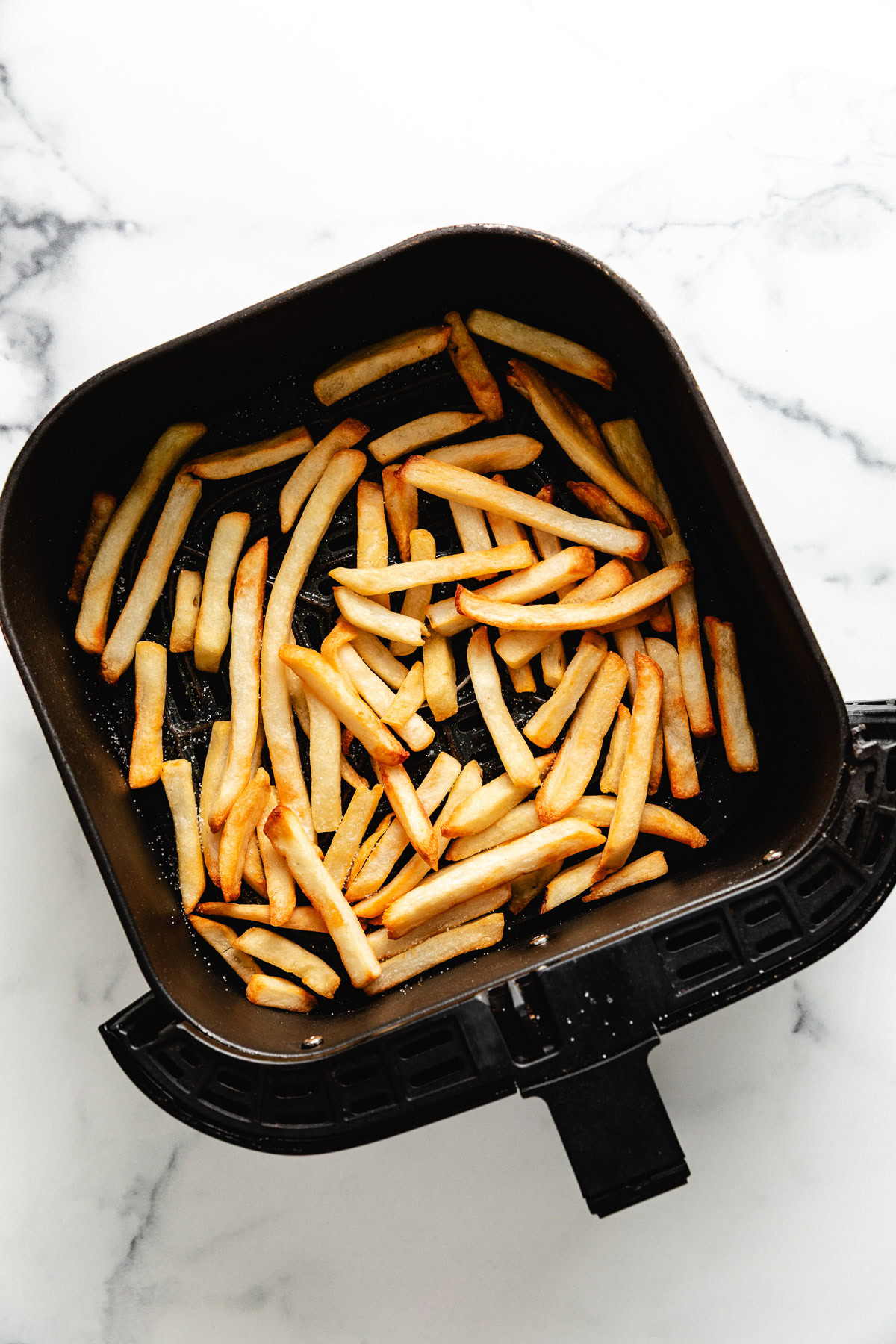 Seasoned french fries in an air fryer basket.