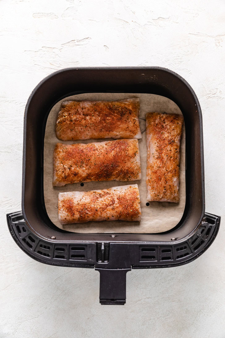 Seasoned mahi mahi fillets in an air fryer basket.